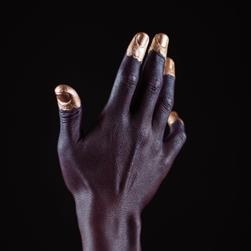 Dark skinned hand with gold fingertips against a black background.